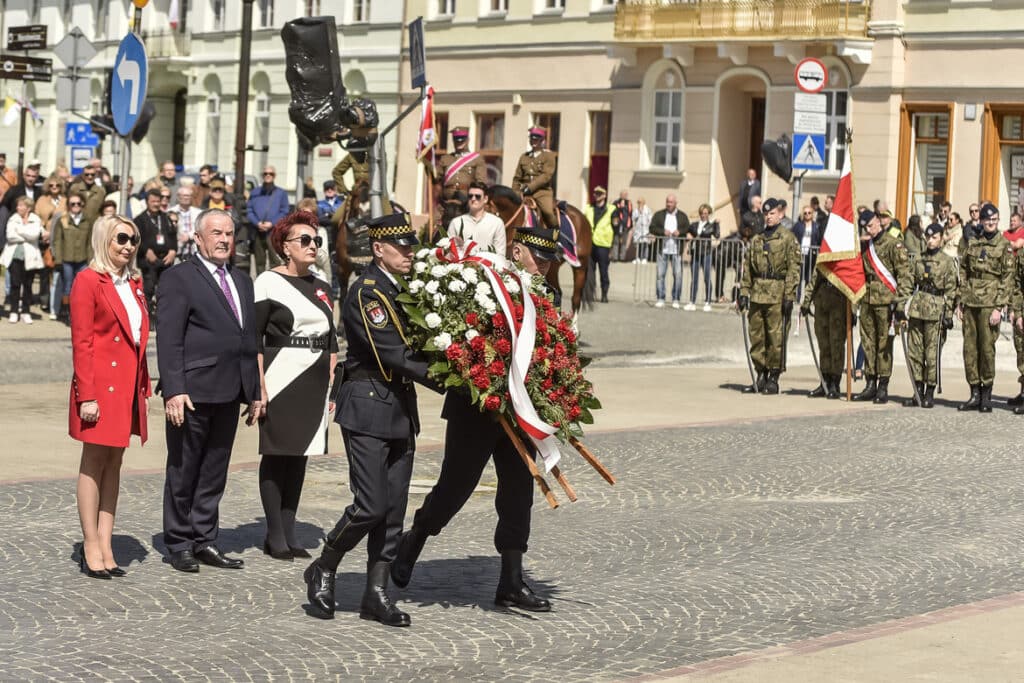 Ceremonia składania wieńca przez przedstawicieli władz i służb mundurowych w obecności zgromadzonych ludzi.
