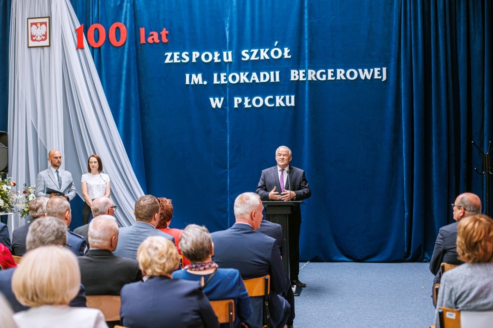 Uroczystość z okazji 100-lecia Zespołu Szkół im. Leokadii Bergerowej w Płocku, z przemawiającym gościem oraz słuchaczami siedzącymi na sali.
