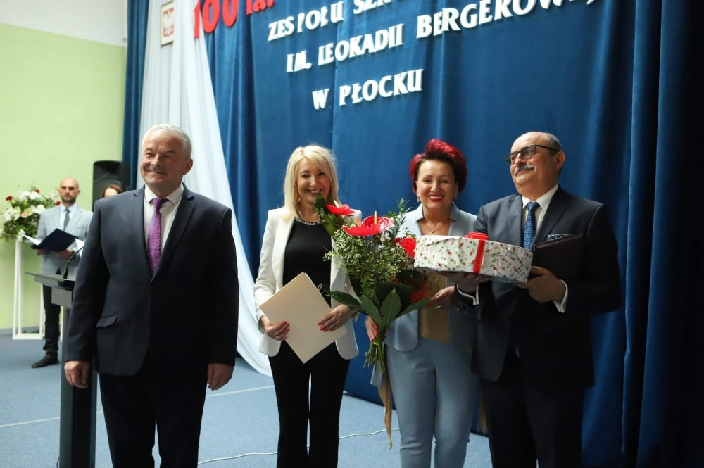 Uroczystość jubileuszu 100-lecia Zespołu Szkół im. Leokadii Bergerowej w Płocku z udziałem uśmiechniętych gości trzymających kwiaty i prezenty.