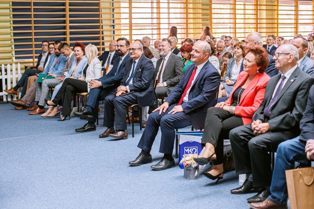 Zdjęcie przedstawia grupę osób siedzących na uroczystości jubileuszowej w sali z oknami, które uczestniczą w wydarzeniu związanym z obchodami 100-lecia zespołu szkół im. Leokadii Bergerowej w Płocku.