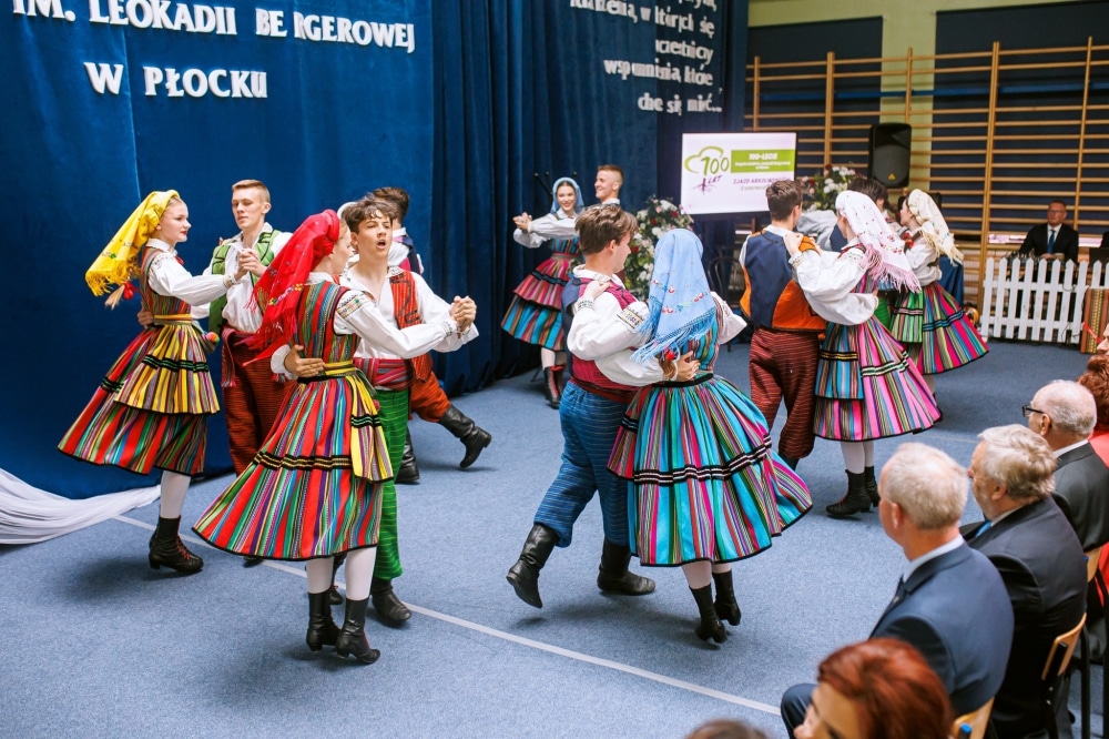 Zdjęcie przedstawia zespół taneczny w kolorowych strojach ludowych, tańczący na uroczystości jubileuszowej w Płocku.