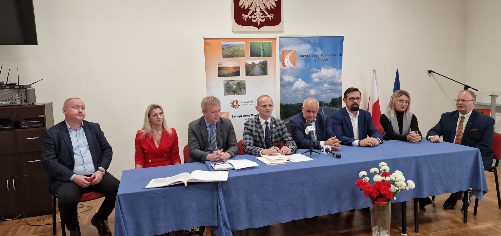 Na zdjęciu przedstawiono grupę osób siedzących przy stole podczas konferencji dotyczącej wyremontowanych dróg w powiecie płockim.
