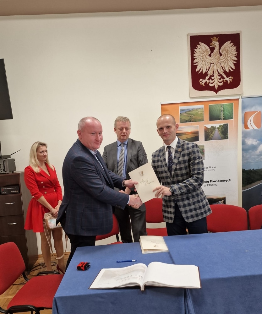 Na zdjęciu czterech mężczyzn i jedna kobieta uczestniczy w ceremonii podpisania umowy dotyczącej remontu dróg w powiecie płockim.