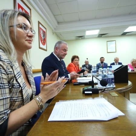 Na zdjęciu przedstawiono zebranie rady powiatu z uczestnikami siedzącymi przy stole oraz osobą prowadzącą obrady.