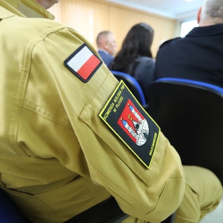 Na zdjęciu widać mundur z naszywkami przedstawiającymi herb oraz flagę Polski, na tle osób uczestniczących w spotkaniu.