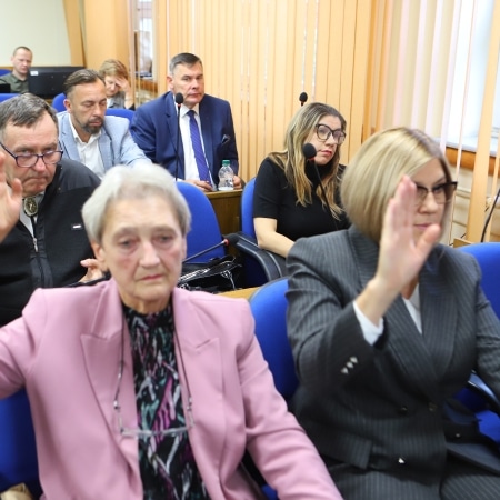 Na zdjęciu widać członków rady powiatu podczas sesji, podnoszących ręce w geście głosowania.