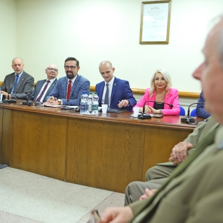 Na zdjęciu przedstawiono członków rady powiatu siedzących przy stole podczas sesji, z wyraźnymi ujęciami mężczyzn w garniturach oraz jednej kobiety w różowej marynarce.