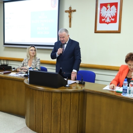 Na zdjęciu przedstawiono sesję Rady Powiatu Płockiego, podczas której mężczyzna przemawia, a obok niego siedzą dwie kobiety.