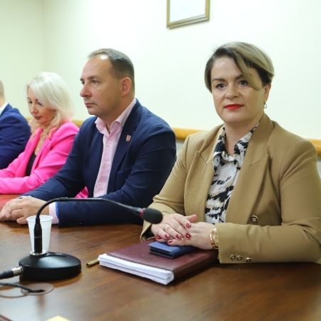 Na zdjęciu widać czwórkę osób siedzących przy stole podczas sesji rady powiatu, w tym kobietę w beżowej marynarce i mężczyznę w granatowym ubraniu.