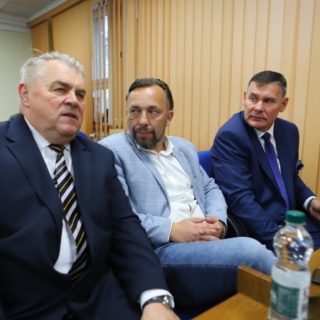 Na zdjęciu widoczna jest grupa trzech mężczyzn siedzących w sali, w trakcie spotkania.