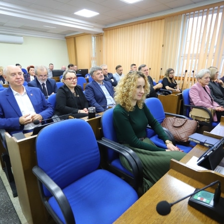 Na zdjęciu widoczna jest sala obrad z uczestnikami sesji rady powiatu, siedzącymi w niebieskich fotelach.
