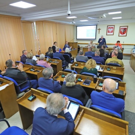 Na zdjęciu przedstawiono spotkanie Rady Powiatu w Płocku, w którym uczestniczy wielu radnych oraz przedstawicieli lokalnych instytucji.