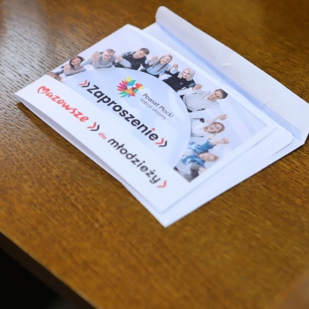 Na zdjęciu znajduje się zaproszenie skierowane do młodzieży, umieszczone na stole, z widoczną grafiką i uśmiechniętymi osobami w tle.