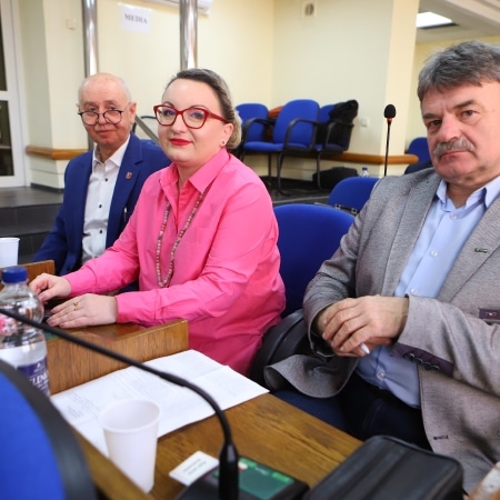 Na zdjęciu widać trzech uczestników sesji Rady Powiatu w Płocku, siedzących przy stole, z widocznymi dokumentami i naczyniami.