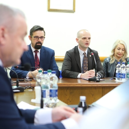 Na zdjęciu przedstawiona jest sesja Rady Powiatu, podczas której uczestnicy dyskutują przy stole, wyposażonym w mikrofony i butelki z wodą.