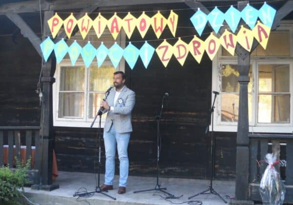 Mężczyzna przemawia na scenie podczas wydarzenia promującego zdrowie w kontekście walki z przemocą, obok kolorowe bannerki z napisami.