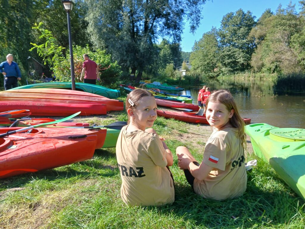 Uczestniczki VI edycji spływu kajakowego w Cierszewie siedzą na trawie obok kolorowych kajaków.