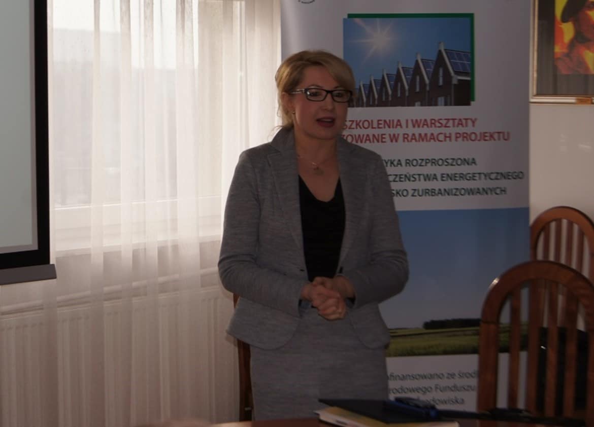 Na zdjęciu widoczna jest kobieta w szarym garniturze, która prowadzi prezentację na temat energetyki rozproszonej w kontekście bezpieczeństwa energetycznego na terenach nisko zurbanizowanych.