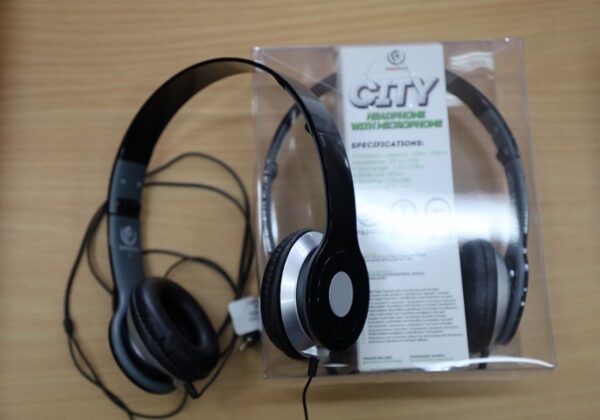 Na zdjęciu znajdują się słuchawki z mikrofonem w opakowaniu, umieszczone na drewnianym blacie.