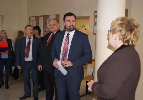 Na zdjęciu widać grupę osób biorących udział w wyjazdowym posiedzeniu Zarządu Powiatu, zgromadzonych w wewnętrznej przestrzeni budynku.