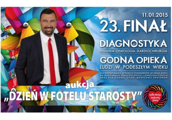 Na zdjęciu prezentowany jest mężczyzna w garniturze z uśmiechem, stojący na tle kolorowej grafiki promującej aukcję na rzecz opieki nad ludźmi w podeszłym wieku organizowaną przez Wielką Orkiestrę Świątecznej Pomocy.