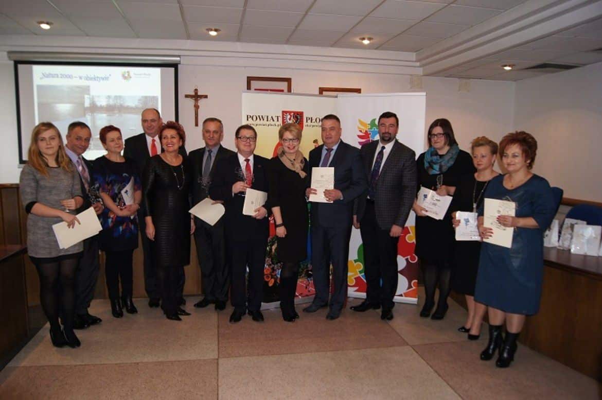 Na zdjęciu grupa osób stoi w sali, trzymając dyplomy i nagrody podczas uroczystości wręczenia „Kwiatów Powiatu”.