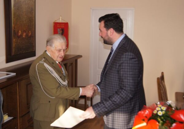 Na zdjęciu widoczny jest Płk Antoni Jelec, który z okazji swoich 90. urodzin serdecznie wita się z mężczyzną w garniturze.