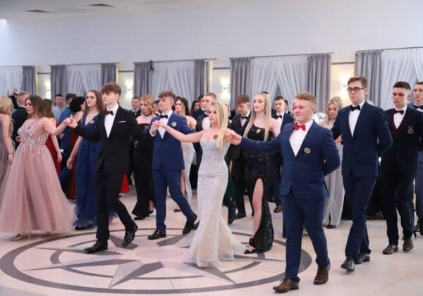 Młodzież w eleganckich strojach tańczy na balu, tworząc kolorową mozaikę stylów i emocji.