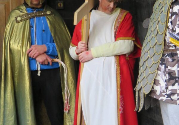 Na zdjęciu widoczna jest scena przedstawiająca postacie w strojach historycznych, w tym postaci z krzyżem oraz żołnierzy z hełmami, stojących w wejściu do budynku.