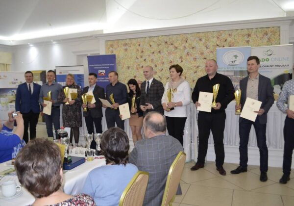 Zdjęcie przedstawia grupę laureatów stojących w sali, trzymających puchary i dyplomy podczas uroczystości wręczenia nagród.