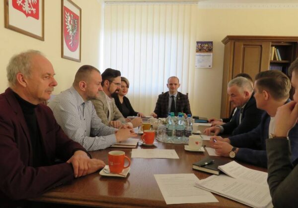 Na zdjęciu znajduje się grupa ludzi siedzących przy stole w biurze podczas spotkania.