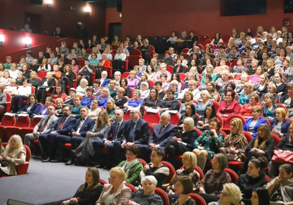 Na zdjęciu widać dużą salę, w której zgromadzeni są uczestnicy wydarzenia, głównie kobiety, siedzący w czerwonych fotelach.
