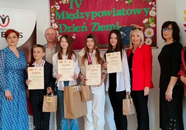 Na zdjęciu przedstawiono grupę osób podczas IV Międzypowiatowego Dnia Ziemi, trzymających dyplomy i nagrody, z kolorowym tłem.