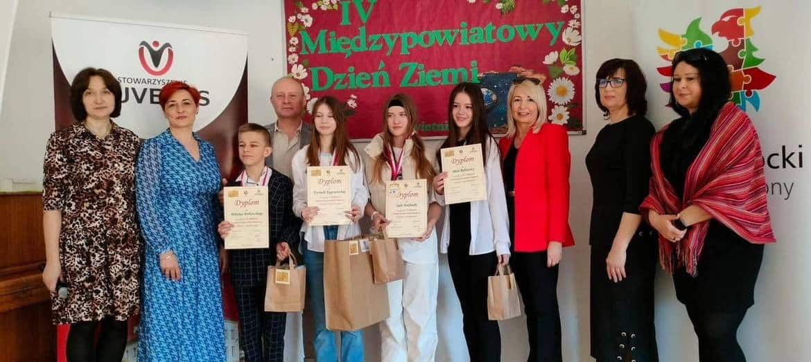 Na zdjęciu przedstawiono grupę osób podczas IV Międzypowiatowego Dnia Ziemi, trzymających dyplomy i nagrody, z kolorowym tłem.