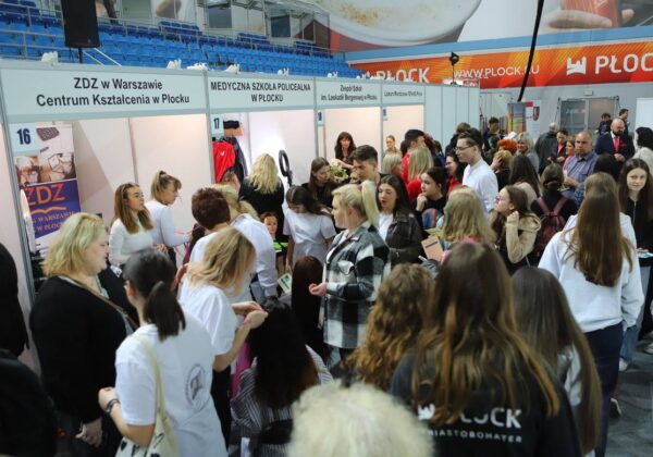Na zdjęciu widać dużą grupę ludzi uczestniczących w targach edukacyjnych w Płocku, z przedstawicielami różnych szkół i instytucji w tle.