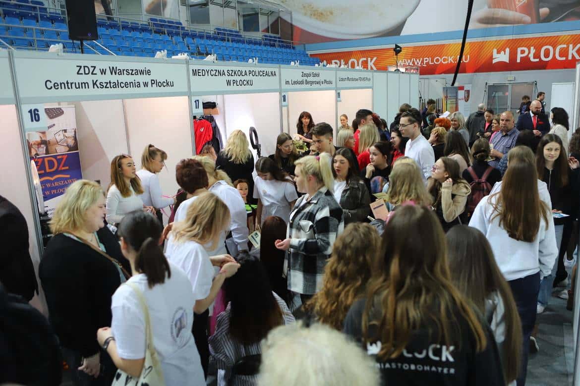 Na zdjęciu widać dużą grupę ludzi uczestniczących w targach edukacyjnych w Płocku, z przedstawicielami różnych szkół i instytucji w tle.