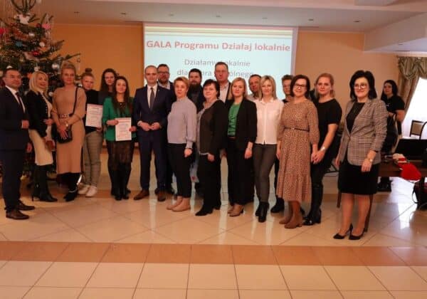 Grupa ludzi podczas gali programu "Działaj lokalnie" w świątecznie udekorowanej sali.