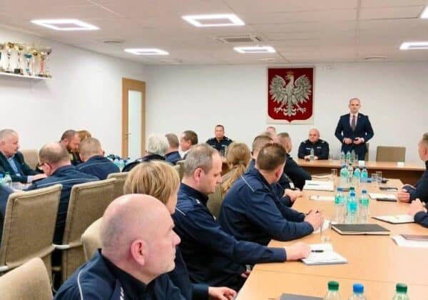 Na zdjęciu widoczna jest sala konferencyjna, w której uczestnicy posiedzenia w mundurach omawiają kwestie związane z bezpieczeństwem, a ich uwagę przyciąga mówiący mężczyzna w garniturze.