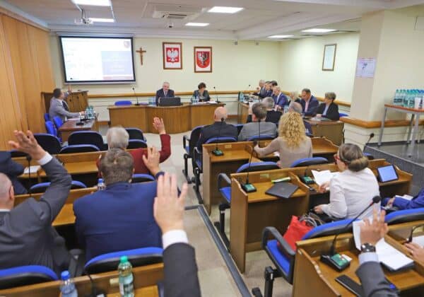 Na zdjęciu przedstawiona jest sala obrad, w której uczestnicy podnoszą ręce podczas głosowania.