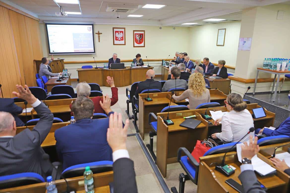 Na zdjęciu przedstawiona jest sala obrad, w której uczestnicy podnoszą ręce podczas głosowania.