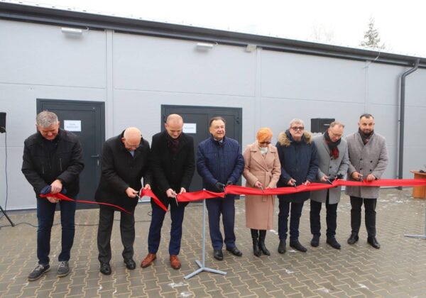 Na zdjęciu grupa ludzi bierze udział w ceremonii przecięcia wstęgi przed nowym obiektem.