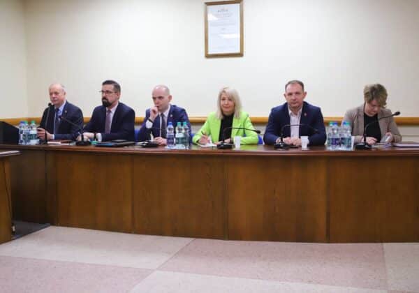 Zdjęcie przedstawia grupę osób siedzących przy stole w sali konferencyjnej, podczas spotkania lub konferencji.