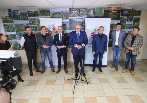 Zdjęcie przedstawia grupę mężczyzn oraz kobietę podczas konferencji prasowej w pomieszczeniu z tłem w postaci zdjęć krajobrazów, z mikrofonami i banerami promocyjnymi.