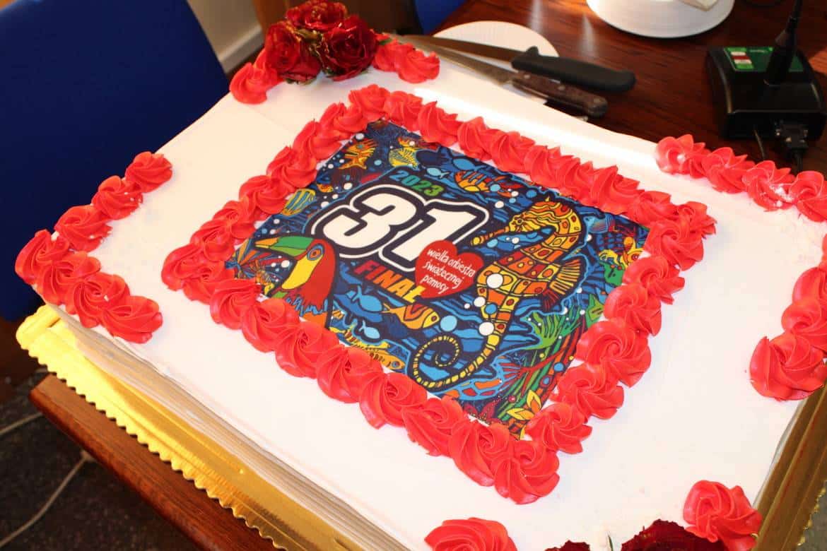 Na zdjęciu znajduje się tort ozdobiony czerwoną polewą i kolorowym nadrukiem z logo 31. Finału Wielkiej Orkiestry Świątecznej Pomocy.