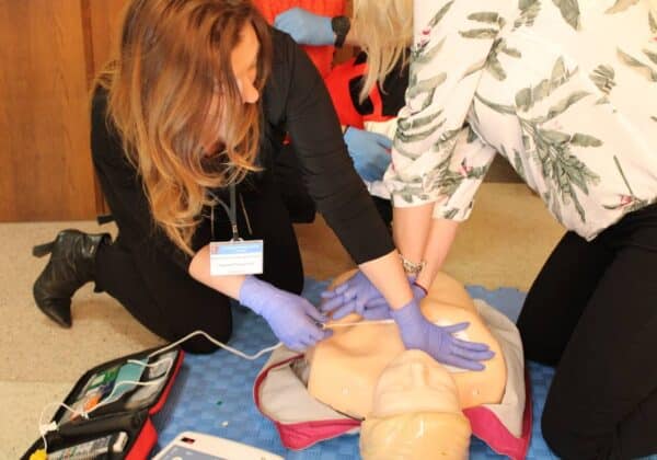 Na zdjęciu dwie kobiety wykonują resuscytację krążeniowo-oddechową na manekinie, stosując się do zasad pierwszej pomocy.
