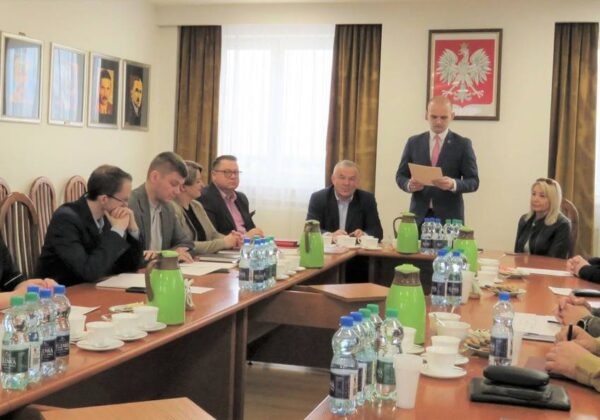 Na zdjęciu widoczna jest grupa osób podczas posiedzenia w sali konferencyjnej, gdzie jeden z uczestników przemawia, a pozostałe osoby słuchają.