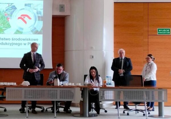 Na zdjęciu przedstawiono spotkanie dotyczące bezpieczeństwa środowiskowego w Zakładzie Produkcyjnym w Płocku, z prelegentami i uczestnikami zgromadzonymi przy stole.