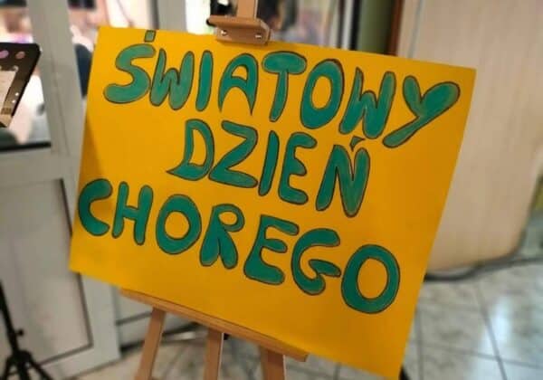 Plakat z napisem "Światowy Dzień Chorego" wyeksponowany na stojaku w jasnym pomieszczeniu.