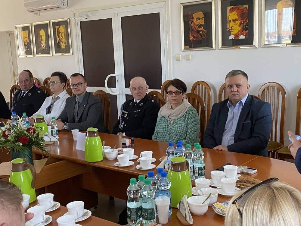 Na zdjęciu przedstawiono grupę osób siedzących przy stole podczas spotkania, z napojami i przekąskami, w pomieszczeniu z obrazami na ścianach.