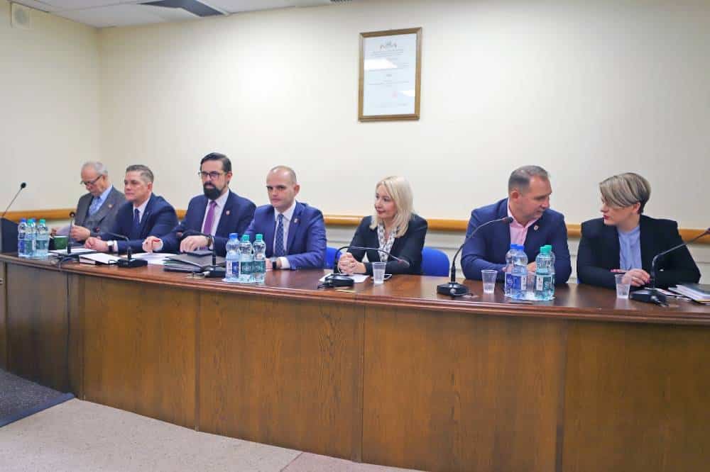 Na zdjęciu widać grupę osób siedzących przy stole w sali obrad, uczestniczących w sesji rady powiatu.